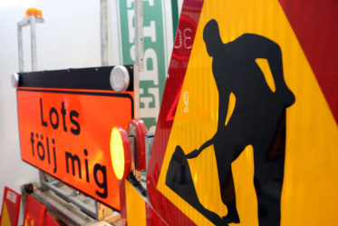 Vägskyltar visar en man som gräver.
Arbete på väg.
Textskylt med texten Lots på väg.